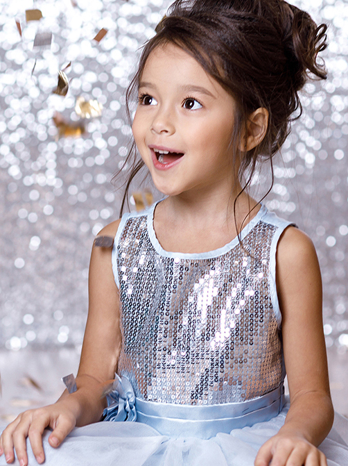 little child girl in blue dress sitting on the floor with confetti on background with silver bokeh. birtday party